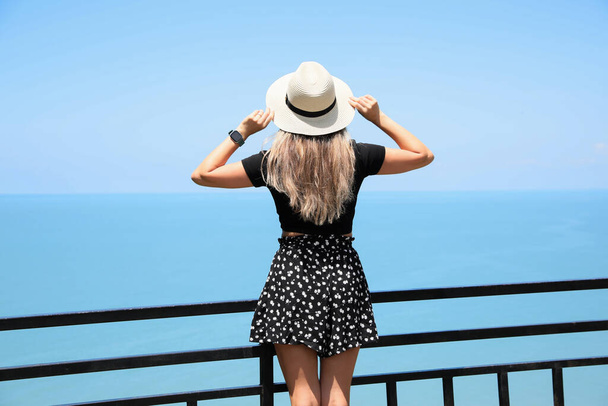 Woman with hat near sea on sunny day, back view - Фото, зображення
