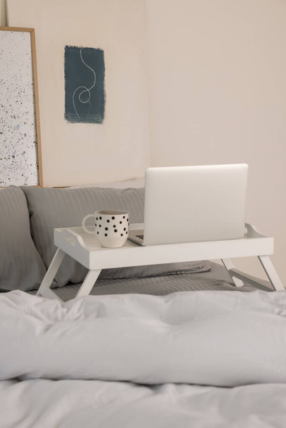 White tray table with laptop and cup of drink on bed indoors - Foto, Bild
