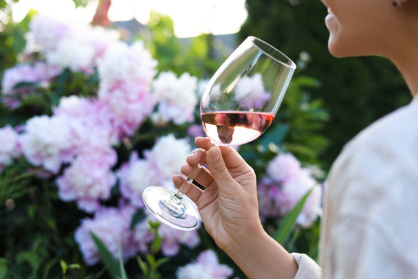 Woman with glass of rose wine in peony garden, closeup - Photo, Image