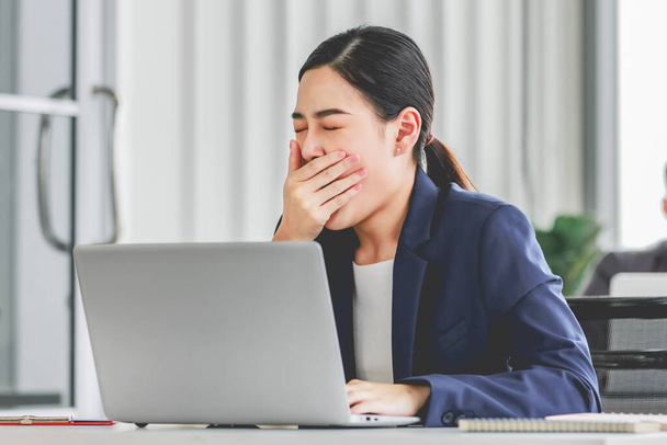 Closeup shot of millennial Asian young stressed depressed sleepy female businesswoman employee sitting holding hand on messy hair working on workstation desk via laptop notebook computer in office. - 写真・画像