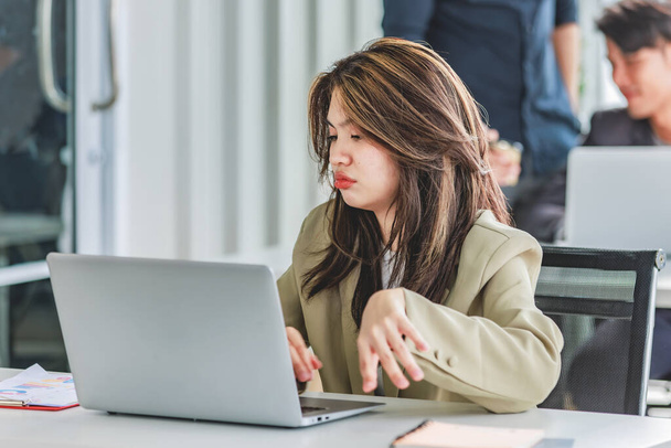Closeup shot of millennial Asian young stressed depressed sleepy female businesswoman employee sitting holding hand on messy hair working on workstation desk via laptop notebook computer in office. - Photo, image