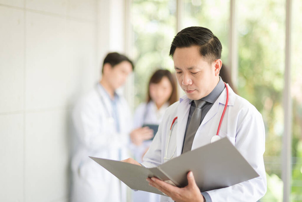 Asian doctor man portrait in professional uniform standing and holding folder to review data with smile and confidence. - Foto, Imagem
