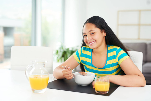 The brightest days start with a healthy breakfast. Portrait of a happy young girl enjoying a healthy breakfast at home - Foto, immagini