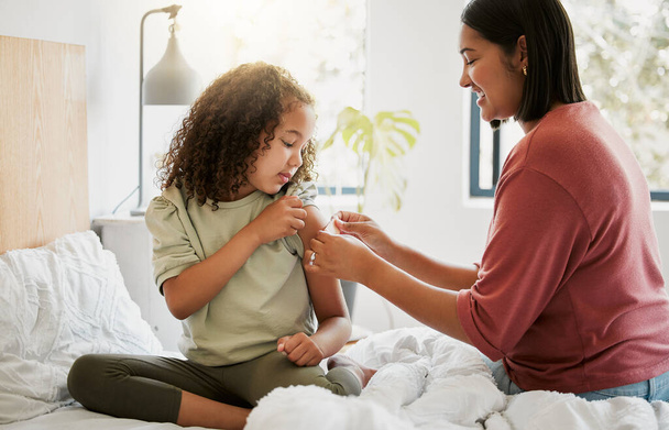 Loving mother comforting her daughter with a bandaid in bed, being affectionate and caring at home. Young parent helping her sick child, applying a plaster and bonding, special moments of motherhood. - Foto, afbeelding
