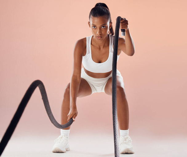 Fit woman doing cardio workout with ropes, exercising for fitness training and looking sporty while posing against a pink studio background. Active and young female athlete doing exercise routine. - 写真・画像
