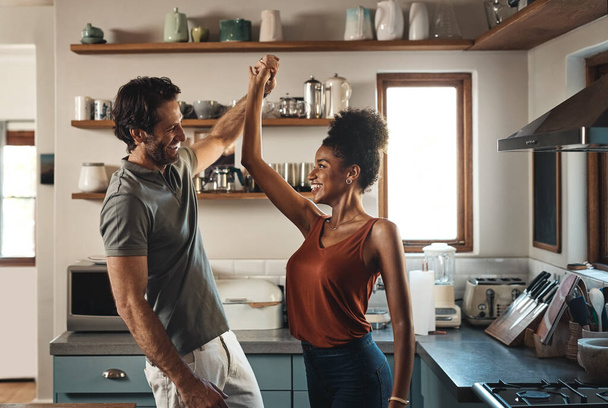 Happy, in love and dancing while an interracial couple have fun and enjoying time together in home kitchen. Husband and wife sharing a dance while being active and affectionate in loving relationship. - Fotó, kép