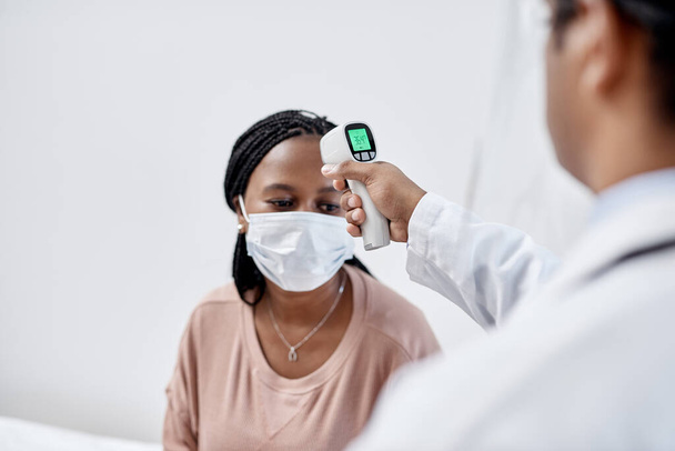 Doctor taking temperature of a covid patient while testing for high fever symptoms of sick, flu or illness. Screening woman for a healthcare consult, checkup and visit in a hospital or medical clinic. - Photo, image