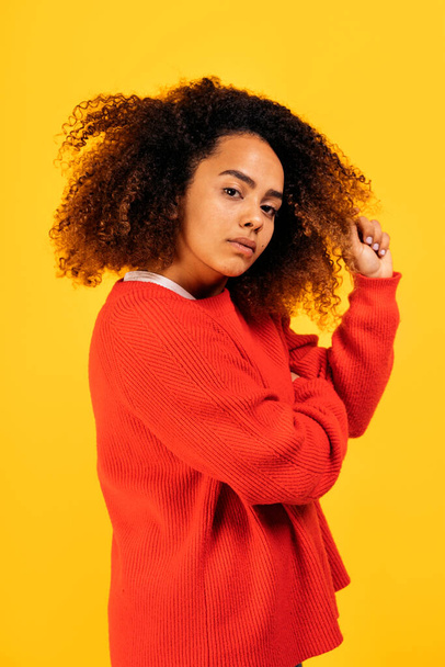 Beautiful black woman with curly hair posing and looking at camera in studio shot against yellow background. - Valokuva, kuva