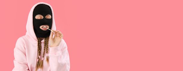 Young woman in balaclava and hoodie chewing gum on pink background with space for text - Foto, Imagen