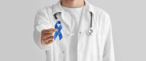 Γιατρός κρατά μπλε κορδέλα στο φως φόντο, κοντινό πλάνο. Έννοια ευαισθητοποίησης για τον καρκίνο του προστάτη - Φωτογραφία, εικόνα
