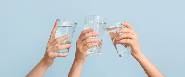 Female hands with glasses of water on light blue background - 写真・画像