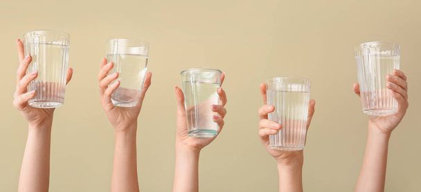 Female hands with glasses of water on beige background - Foto, imagen