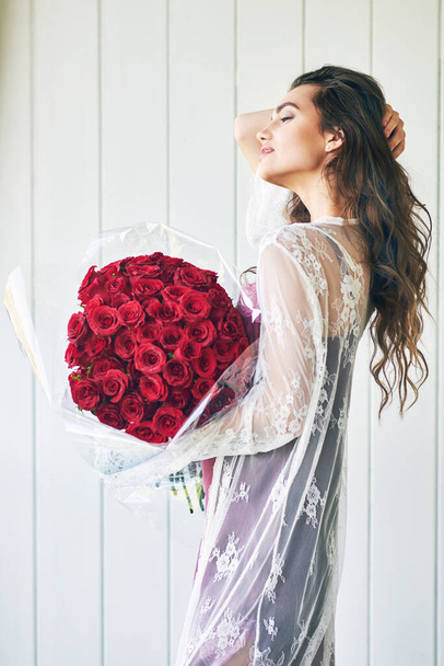 The flowers isnt the only pretty thing here. a beautiful young woman standing with her eyes closed while holding a bouquet of roses outside during the day - Zdjęcie, obraz