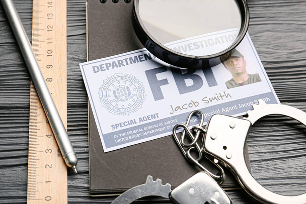 Document of FBI agent with handcuffs, magnifier and stationery on dark wooden background - Foto, afbeelding