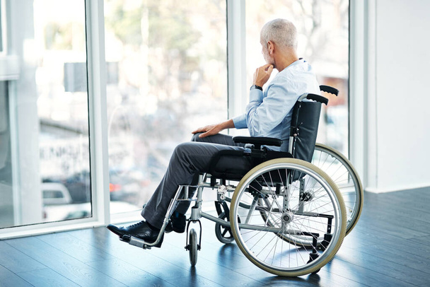 Taking a moment to ponder by himself. a mature man sitting in a wheelchair and looking out the window - 写真・画像