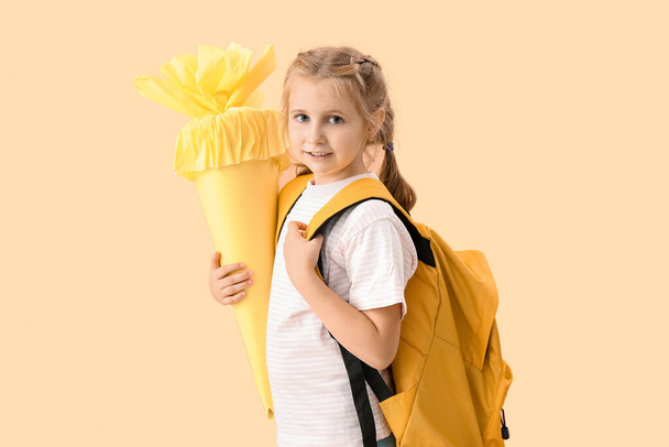 Cute little girl with yellow school cone and backpack on beige background - Foto, Bild
