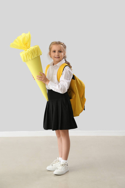 Χαριτωμένο κοριτσάκι με κίτρινο κώνο σχολείο κοντά στο φως τοίχο - Φωτογραφία, εικόνα