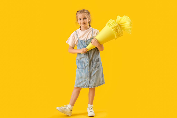 Cute little girl with school cone on yellow background - Φωτογραφία, εικόνα