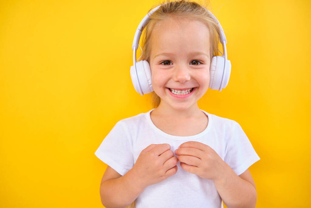 Positive happy little girl listening music in headphones dancing while listening to music on smartphone yellow background  - Fotografie, Obrázek