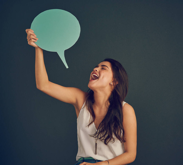 Can you read what Im saying. Studio shot of a cheerful young woman holding up a speech bubble while standing against a dark background - Fotoğraf, Görsel