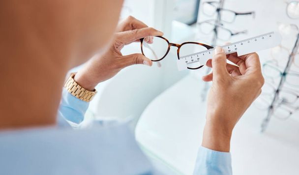 Оптик или оптометрист руки измерения и подготовки пары очков и рамы с помощью оптической линейки инструмента. Глазной врач или офтальмолог определяет размер визуальных или зрительных линз с помощью специальной шкалы очков - Фото, изображение
