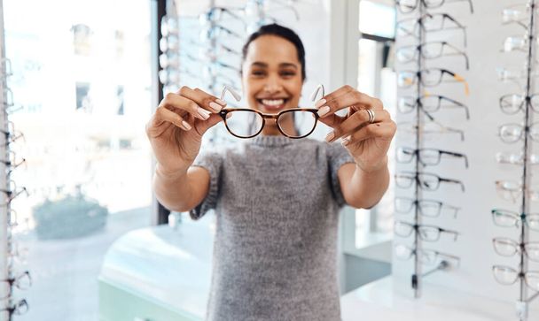 Female holding pair of trendy new glasses, stylish spectacles and prescription lenses at an optometrist. Portrait of a customer choosing, buying and shopping for frames for better vision and eyesight. - Foto, imagen