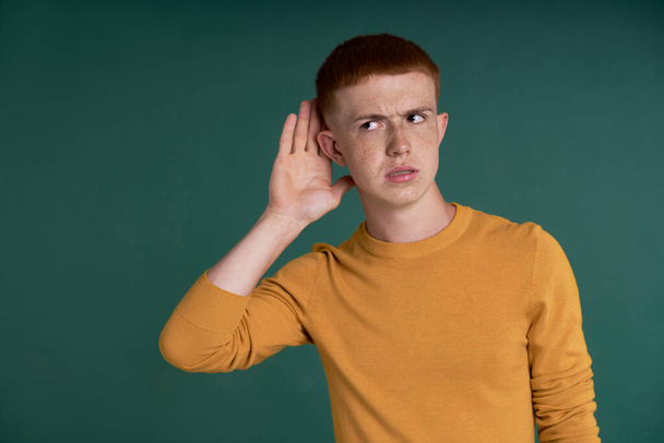 Caucasian teenage boy eavesdropping on green background - Fotó, kép