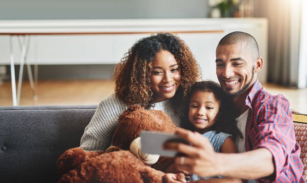 Family time is the best time for a selfie. an adorable little girl taking selfies with her parents at home on a mobile phone - Foto, Imagen