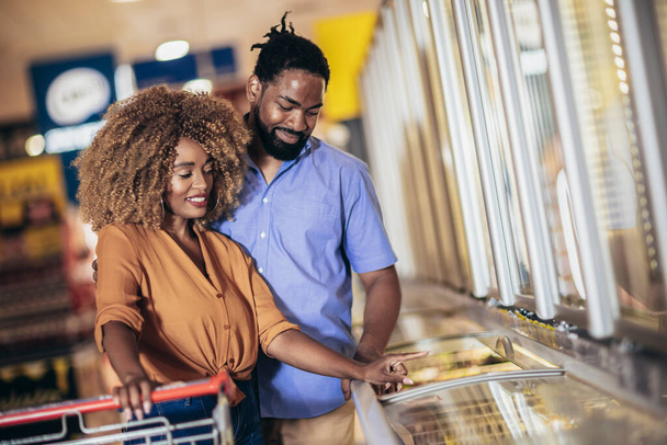 African American couple with trolley purchasing groceries at mall - Foto, Bild