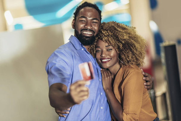 Portrait of smiling black couple showing credit credit card walking in the city shopping mall or supermarket. - Foto, imagen