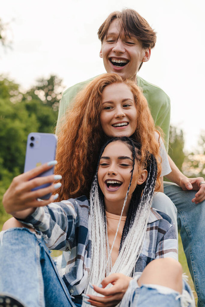 Три современных друга играют видеоблог в социальных сетях в летнем парке. Счастливые дети играют и учатся дома. - Фото, изображение