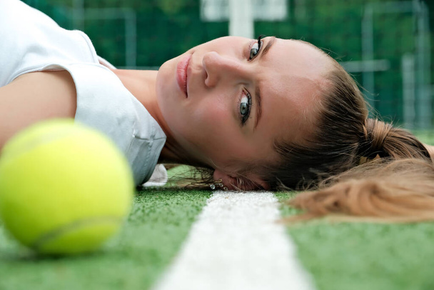 Девушка в белом спортивном платье лежит на теннисном корте. теннисный корт и ракетка. - Фото, изображение