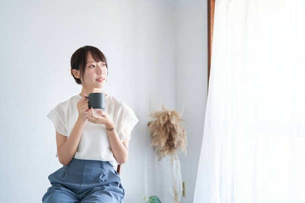 A woman with mug relaxing in a simple space - 写真・画像