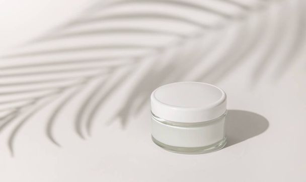 Cream jar with a blank white lid on white close up, Palm leaf hard shadow. Cosmetic packaging Mockup. Exotic natural cosmetics, monochrome composition, everyday skincare routin - Zdjęcie, obraz