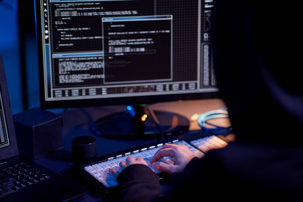 cybercrime, hacking and technology concept - close up of hacker in dark room writing code or using computer virus program for cyber attack - Φωτογραφία, εικόνα