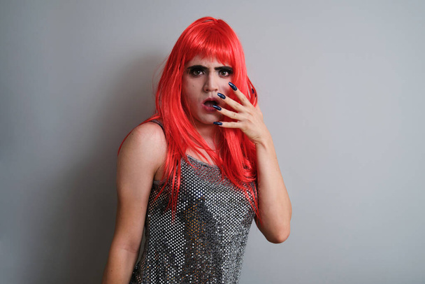 Portrait of drag queen astonished wearing a red wig and looking at camera on grey background. LGBTQ queer. - Photo, image