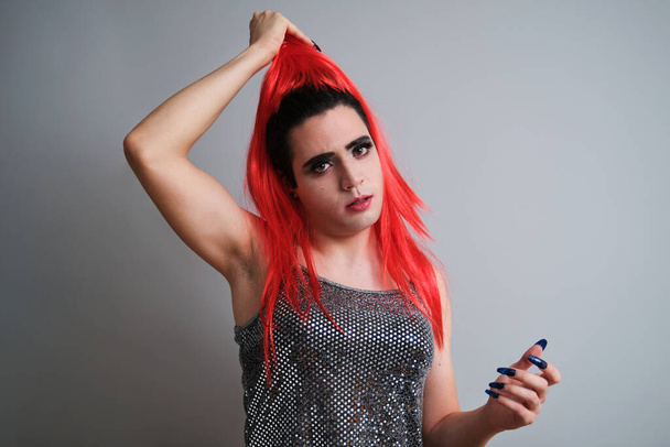 Portrait of drag queentaking off red wig and looking at camera on grey background. LGBTQ queer. - Φωτογραφία, εικόνα