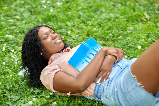 education, school and people concept - happy smiling african american student girl with math textbook lying on grass - Fotografie, Obrázek