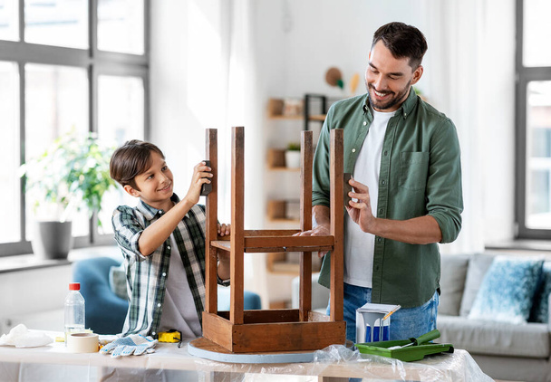 renovação de móveis, diy e conceito de melhoria de casa - feliz sorrindo pai e filho lixar velha mesa redonda de madeira com esponja em casa - Foto, Imagem