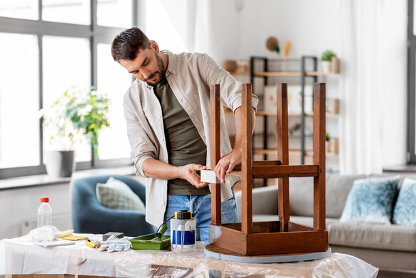 koncept opravy, diy a vylepšení domácnosti - muž lepení lepicí pásky na starý dřevěný stůl pro jeho přemalování - Fotografie, Obrázek