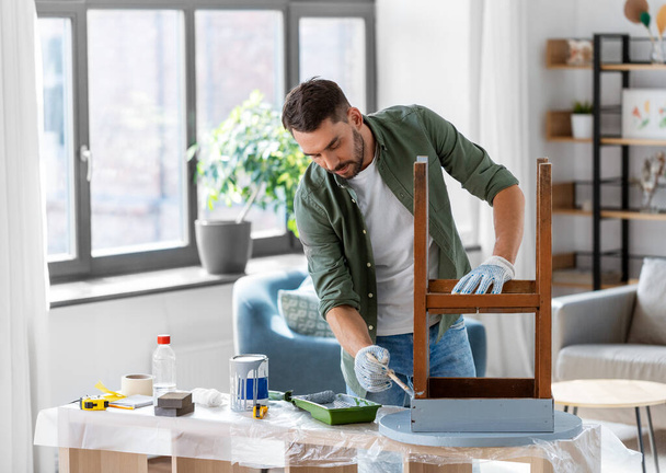 furniture renovation, diy and home improvement concept - man in gloves with paint brush painting old wooden table in grey color - 写真・画像