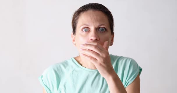 Young beautiful woman surprised and shocked closes mouth with hand. Portrait of frightened woman - Video