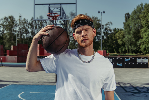 basketball player in bandana and necklace holding ball and looking at camera - Zdjęcie, obraz