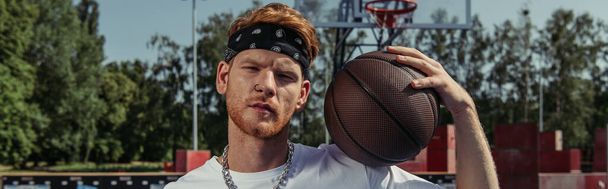 redhead basketball player in headband holding ball and looking at camera, banner - 写真・画像