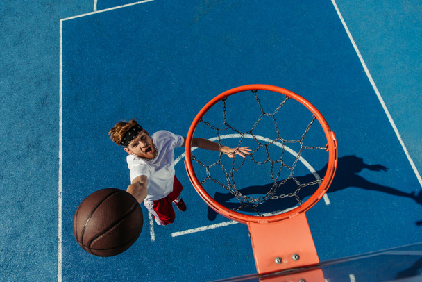 top view of young excited man throwing ball into basketball ring - Fotó, kép