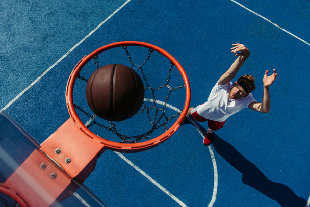 top view of ball in basketball ring and young man training on court - Foto, Imagen