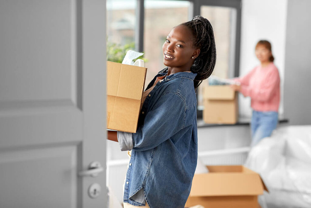moving, people and real estate concept - happy smiling women with boxes at new home - Foto, Bild