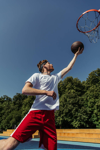 άποψη χαμηλή γωνία του ανθρώπου στα αθλητικά πετώντας μπάλα στο στεφάνι μπάσκετ - Φωτογραφία, εικόνα