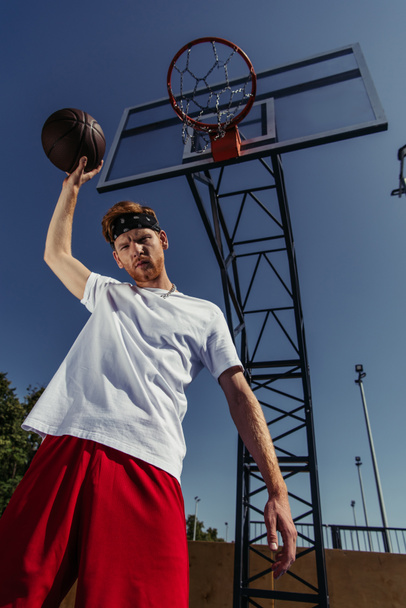 low angle view of sportsman in white t-shirt standing under basketball ring - Фото, зображення