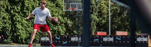 полная длина молодого спортсмена, играющего в баскетбол на площадке, баннер - Фото, изображение